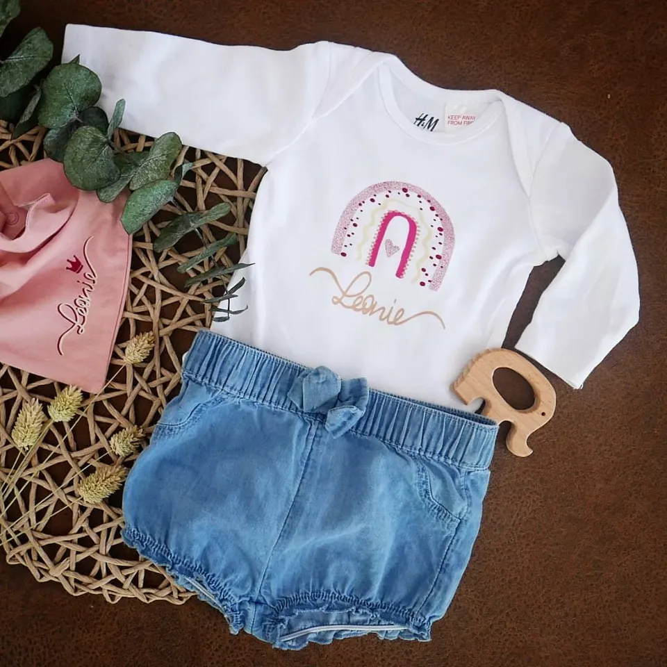 Babybody mit Regenbogen und dem Namen Leonie, dazu Mütze und Shorts