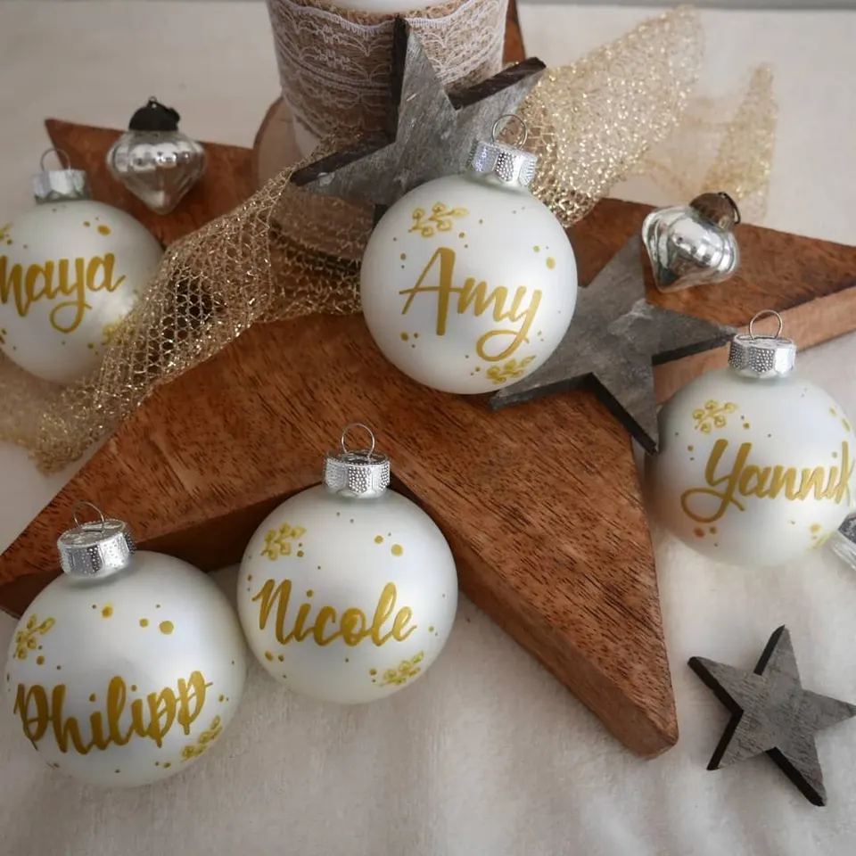Weiße Christbaumkugeln mit goldenen Namen auf einem Holzstern