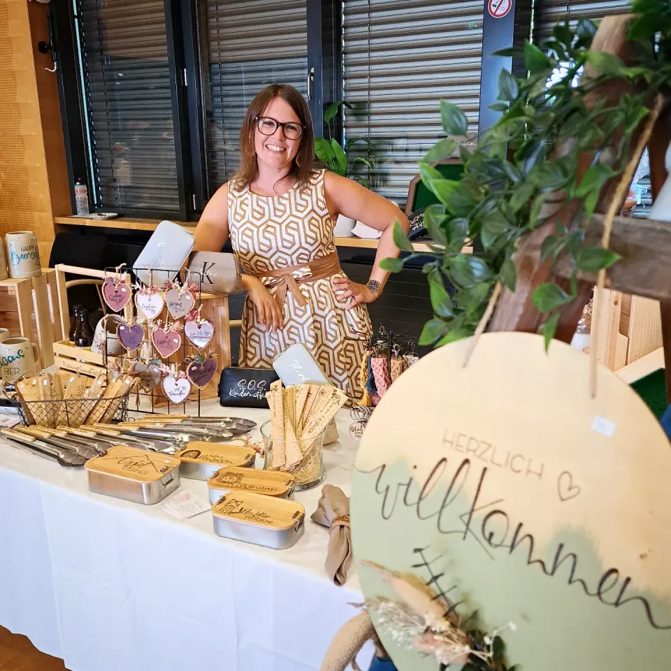 Katharina-Sophie Zotter an ihrem Marktstand, davor ein rundes Holzschild mit Herzlich willkommen