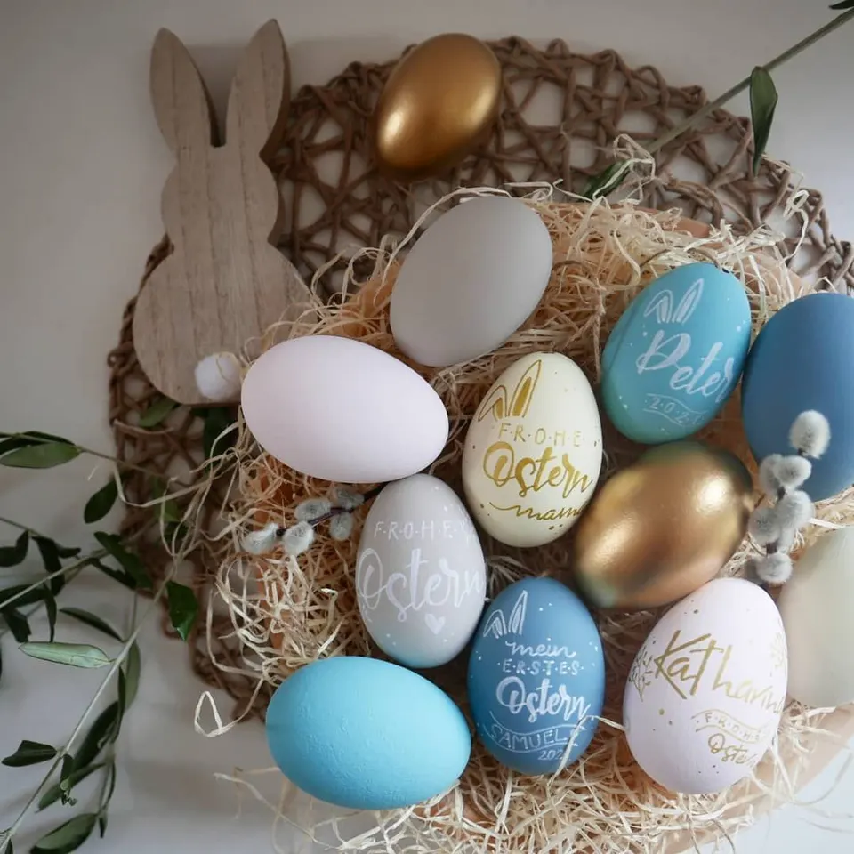 Bunte Gänseeier mit Namen und Frohe Ostern neben einem Holzhasen