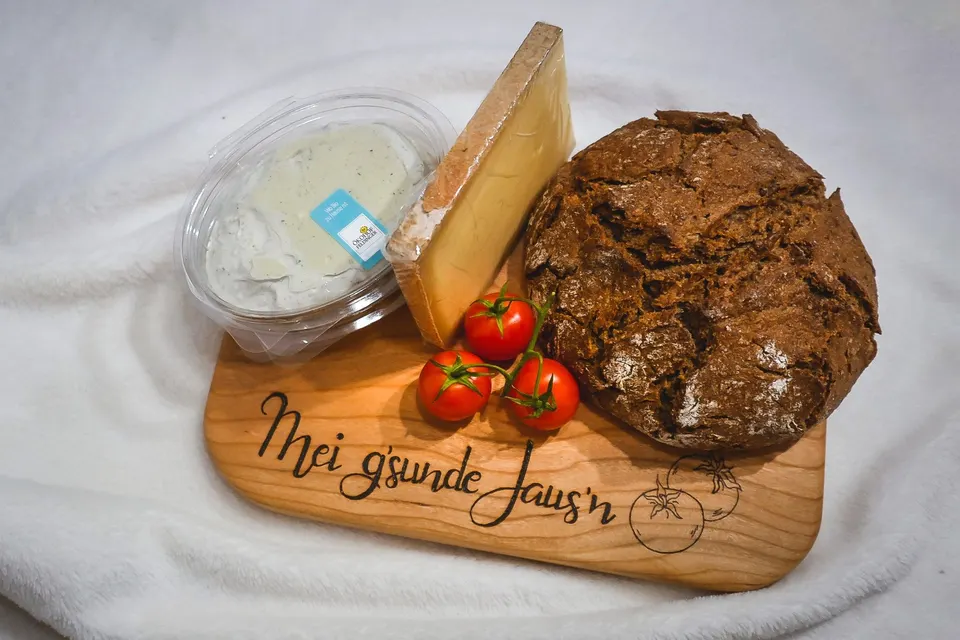 Jausenbrett mit dem Schriftzug Mei g'sunde Jaus'n, darauf Brot, Käse und Tomaten