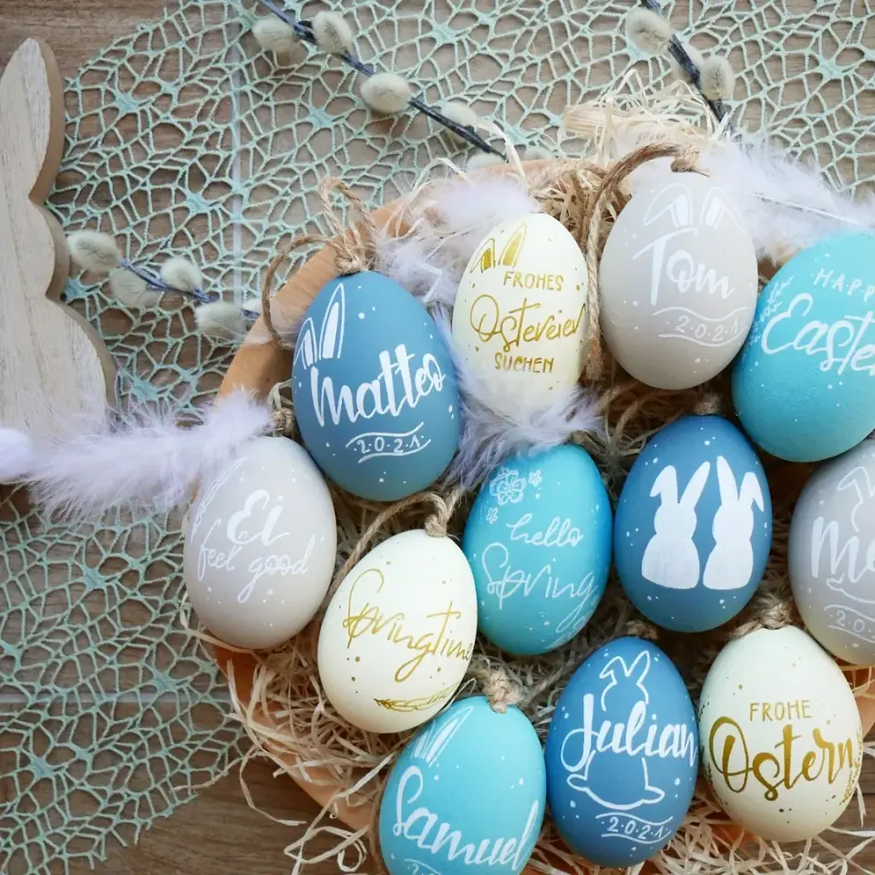 Ostereier in Blau- und Weißtönen mit Namen und Frohe Ostern im Nest