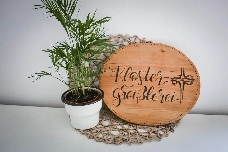 Rundes Holzschild mit dem Schriftzug Kloster-Greißlerei