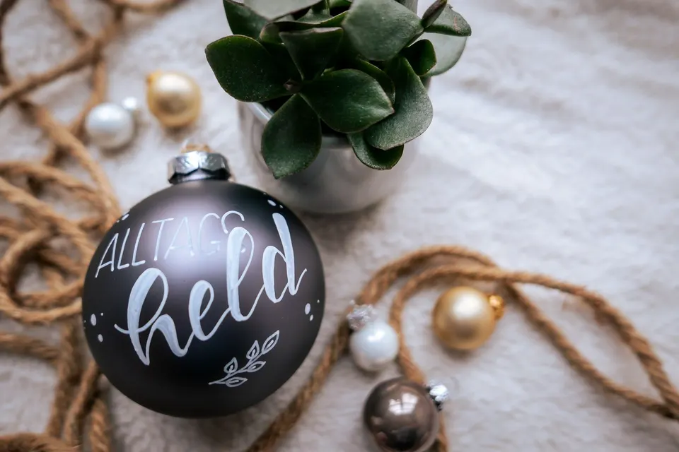 Dunkle Christbaumkugel mit dem Wort Alltagsheld in weißer Schrift