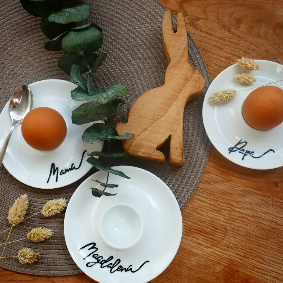 Drei Eierbecher mit Mama, Papa und Magdalena neben einem Holzhasen