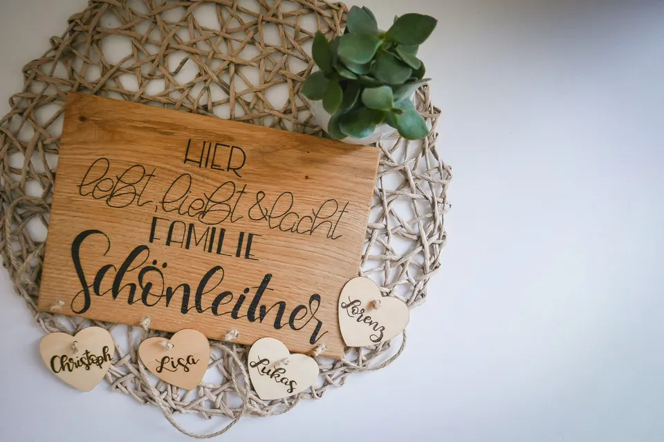 Holzschild Hier lebt, liebt und lacht Familie Schönleitner, daran Holzherzen mit Vornamen