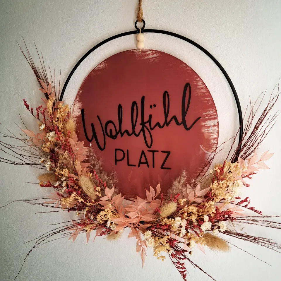 Schwarzer Metallring mit Trockenblumen und einem roten Holzschild Wohlfühlplatz