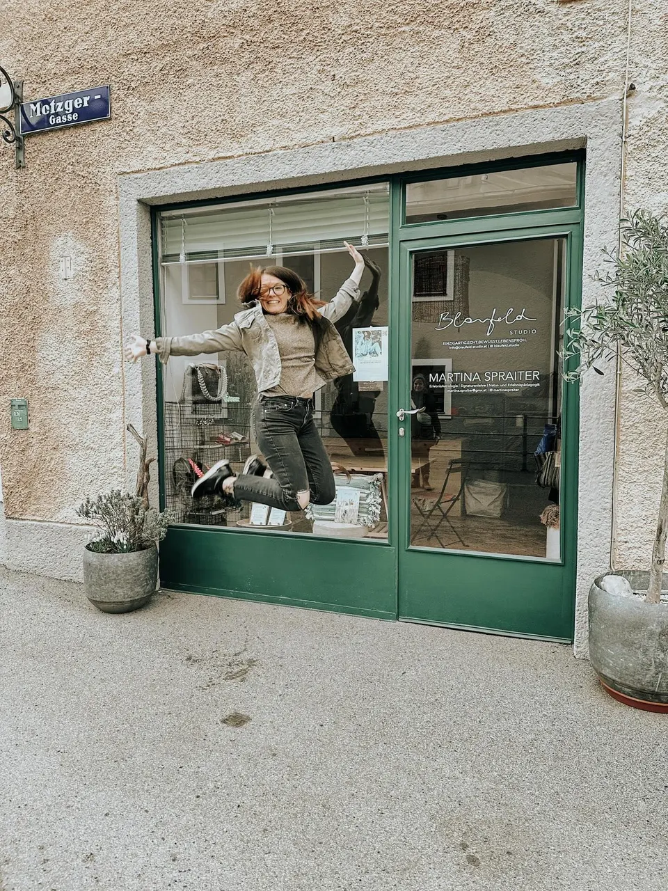 Katharina-Sophie springt vor der grünen Glasfront des one.of.a.kind Concept Studio in der Metzgergasse in Hallein